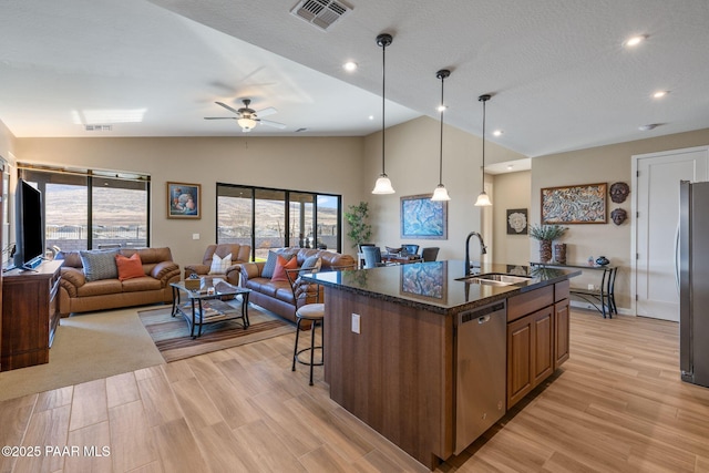 kitchen with sink, appliances with stainless steel finishes, a kitchen island with sink, a kitchen breakfast bar, and decorative light fixtures