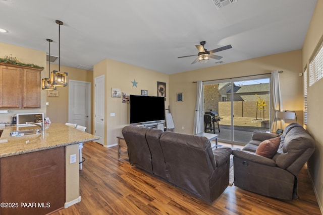 living room featuring ceiling fan with notable chandelier, visible vents, baseboards, and dark wood finished floors