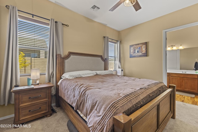 bedroom with a sink, visible vents, ceiling fan, light carpet, and ensuite bath