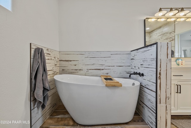 bathroom featuring hardwood / wood-style floors, vanity, wood walls, and a tub to relax in