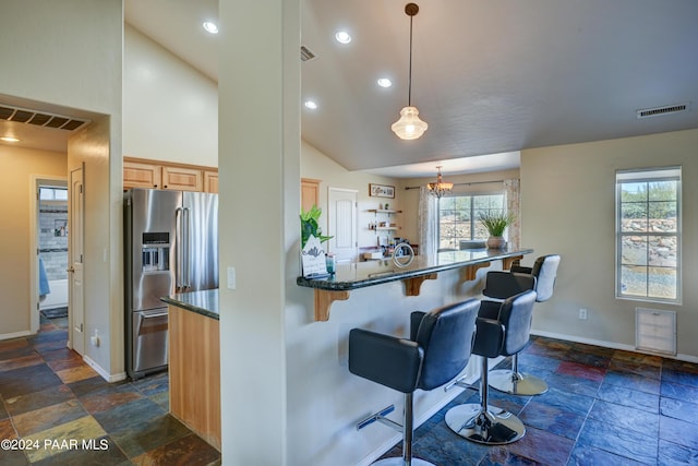 kitchen with dark stone counters, a kitchen breakfast bar, hanging light fixtures, stainless steel fridge with ice dispenser, and a chandelier