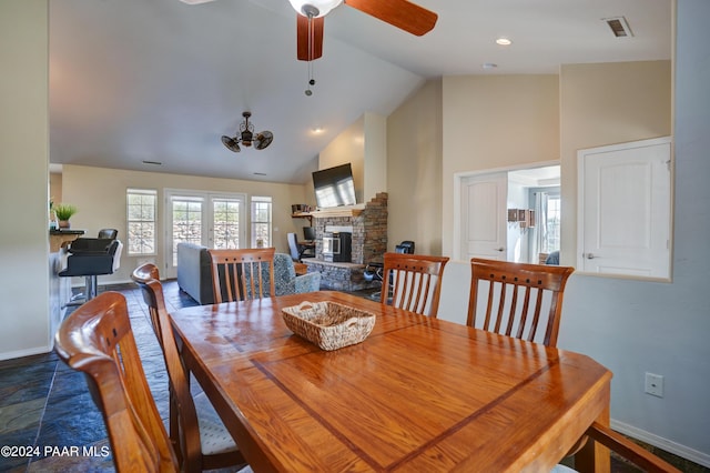 dining space featuring a stone fireplace, ceiling fan, and high vaulted ceiling