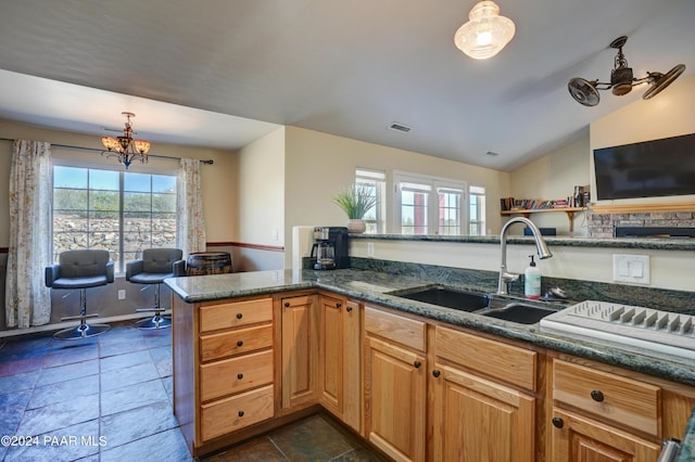 kitchen with sink, kitchen peninsula, dark stone counters, decorative light fixtures, and lofted ceiling