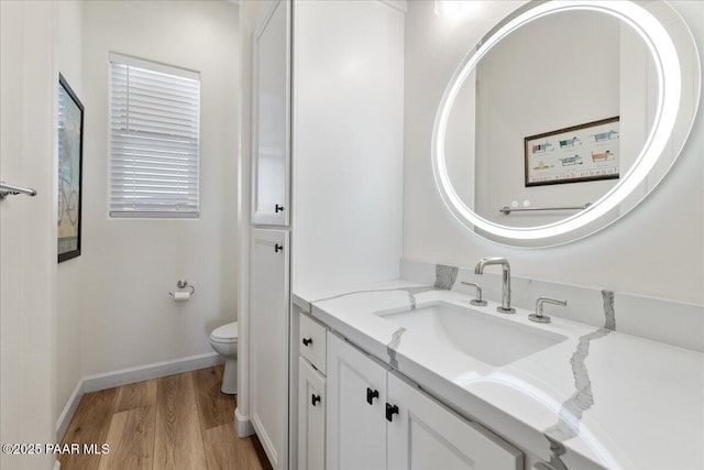 bathroom featuring toilet, baseboards, wood finished floors, and vanity