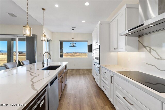 kitchen featuring a sink, visible vents, appliances with stainless steel finishes, light stone countertops, and wall chimney exhaust hood