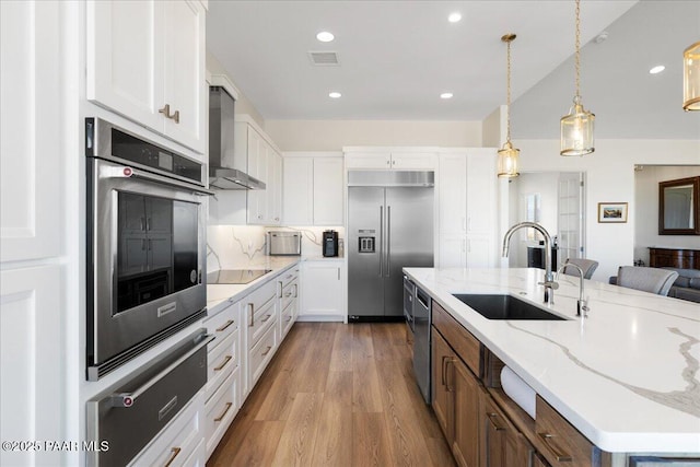 kitchen featuring visible vents, appliances with stainless steel finishes, wall chimney range hood, white cabinetry, and a sink