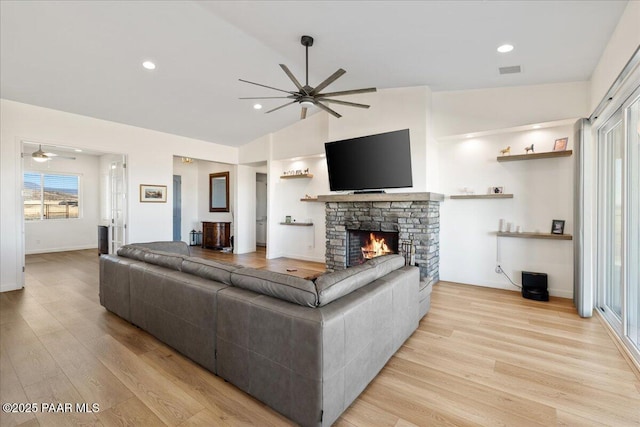 living room featuring lofted ceiling, ceiling fan, a fireplace, and light wood-style flooring