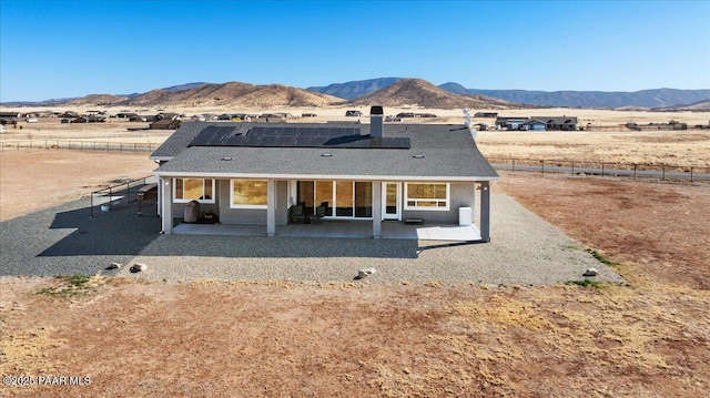 back of house with a patio area, fence, a mountain view, and roof mounted solar panels