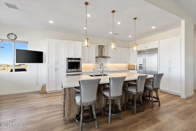 kitchen with white cabinets, stainless steel appliances, light wood-type flooring, wall chimney range hood, and backsplash