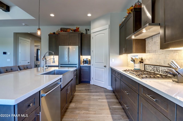 kitchen featuring sink, hanging light fixtures, wall chimney exhaust hood, light wood-type flooring, and stainless steel appliances