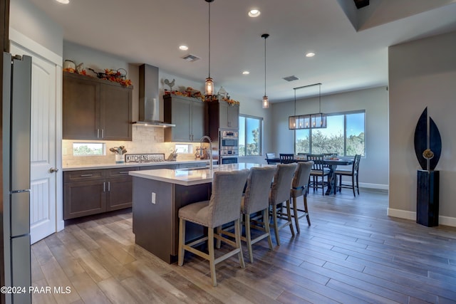 kitchen with sink, wall chimney exhaust hood, a center island with sink, and light wood-type flooring