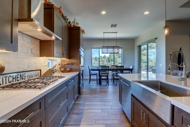 kitchen featuring wood-type flooring, pendant lighting, wall chimney range hood, and appliances with stainless steel finishes