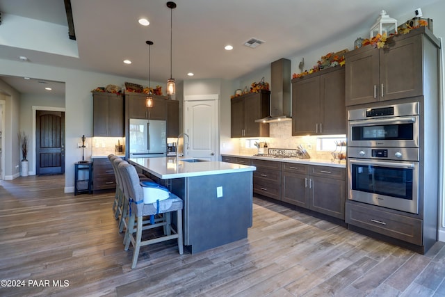 kitchen featuring hardwood / wood-style floors, a center island with sink, appliances with stainless steel finishes, and wall chimney range hood