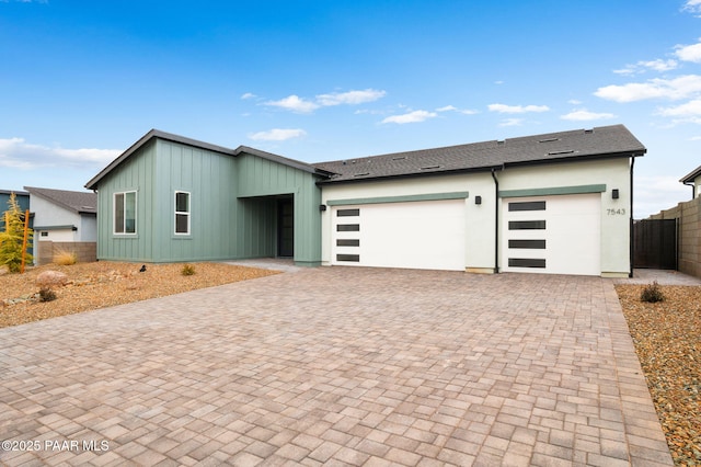 view of front of home with a garage, decorative driveway, a shingled roof, and fence