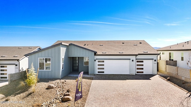 view of front of home featuring an attached garage, decorative driveway, board and batten siding, and fence