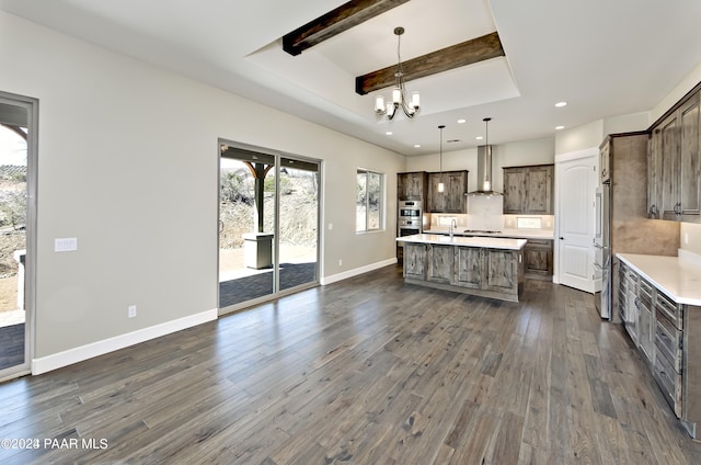 kitchen with dark hardwood / wood-style floors, pendant lighting, a kitchen island with sink, stainless steel appliances, and wall chimney range hood