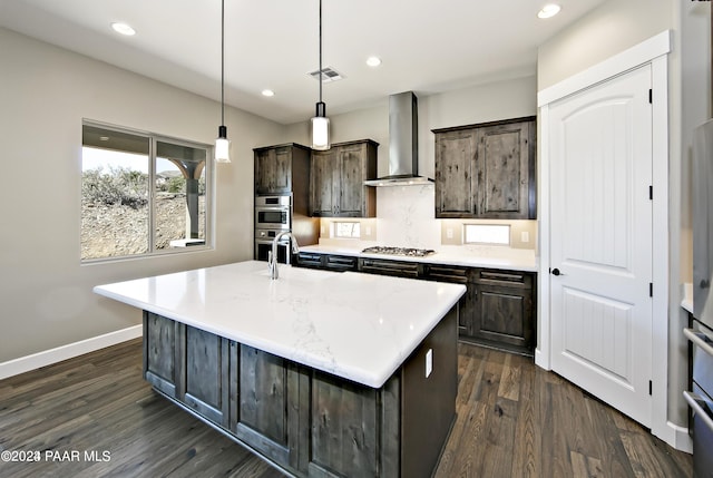 kitchen with pendant lighting, stainless steel gas cooktop, wall chimney exhaust hood, and an island with sink