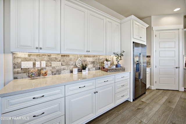 kitchen with stainless steel fridge, light stone countertops, white cabinets, decorative backsplash, and light wood-type flooring