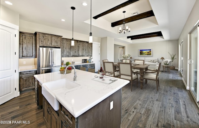 kitchen with pendant lighting, an island with sink, sink, stainless steel fridge, and dark wood-type flooring