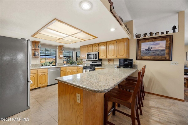 kitchen featuring kitchen peninsula, a kitchen breakfast bar, light stone counters, stainless steel appliances, and light tile patterned floors