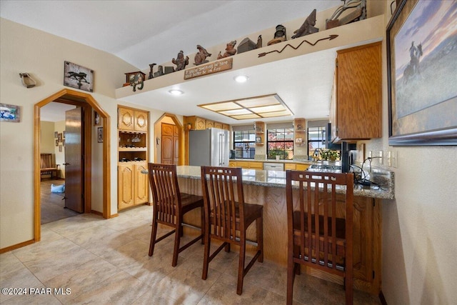 kitchen featuring kitchen peninsula, appliances with stainless steel finishes, a breakfast bar, lofted ceiling, and light tile patterned flooring