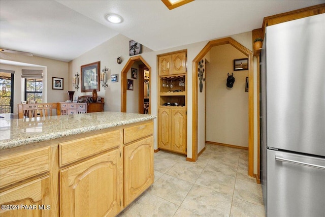 kitchen featuring light stone countertops, ceiling fan, stainless steel fridge, light brown cabinetry, and light tile patterned flooring