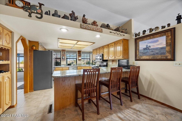 kitchen featuring stainless steel appliances, light stone counters, kitchen peninsula, a breakfast bar, and light tile patterned floors