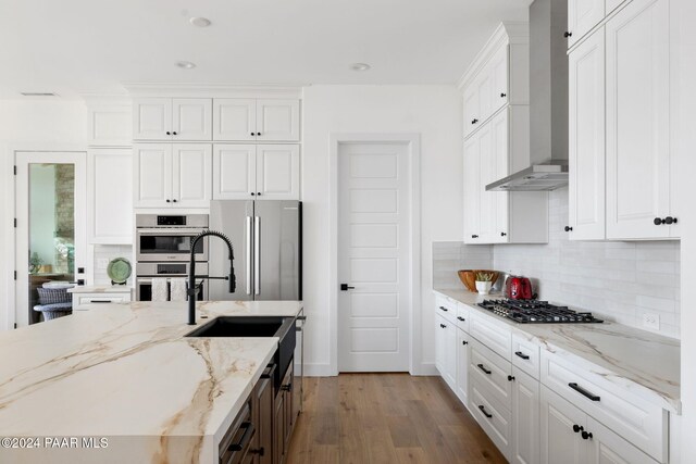 kitchen with white cabinetry, stainless steel appliances, wall chimney range hood, light stone counters, and light hardwood / wood-style floors