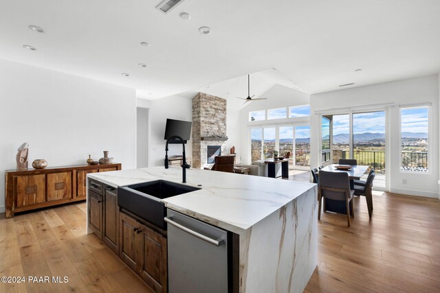 kitchen featuring stainless steel dishwasher, a kitchen island with sink, sink, light hardwood / wood-style flooring, and a stone fireplace