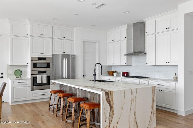 kitchen featuring white cabinets, an island with sink, light hardwood / wood-style floors, and wall chimney range hood