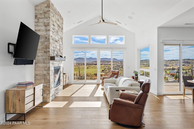 living room with a stone fireplace, ceiling fan, high vaulted ceiling, and a healthy amount of sunlight