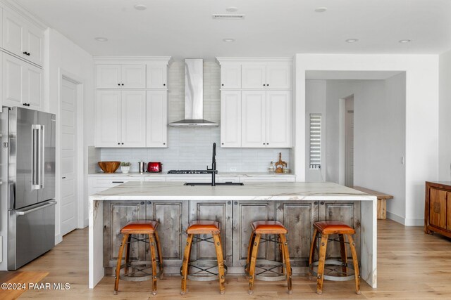 kitchen featuring a kitchen bar, a kitchen island with sink, high end fridge, and wall chimney range hood