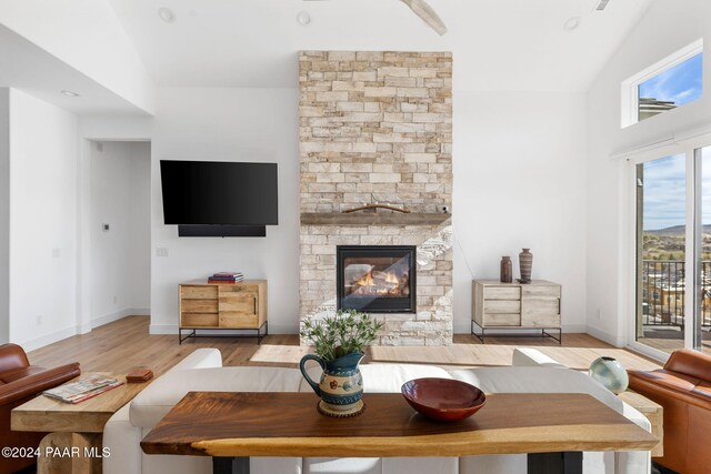 living room featuring light wood-type flooring, high vaulted ceiling, and a stone fireplace