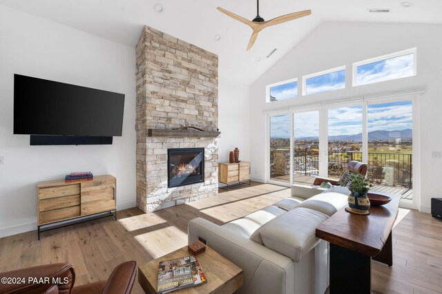 living room with high vaulted ceiling, a stone fireplace, light wood-type flooring, and a wealth of natural light