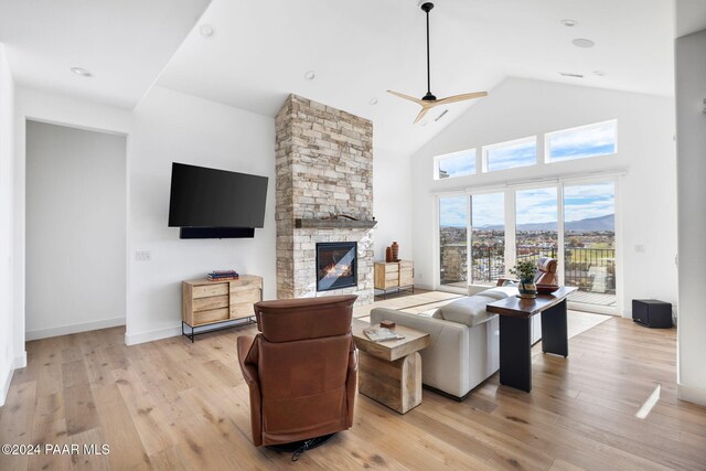 living room featuring ceiling fan, a stone fireplace, light wood-type flooring, and high vaulted ceiling