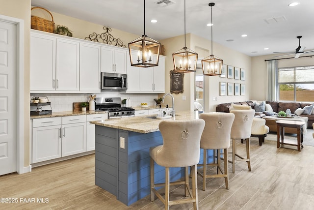 24757 N 175th Dr, Surprise, AZ 85387 - kitchen with decorative backsplash, light wood-style floors, an island with sink, appliances with stainless steel finishes, and a kitchen bar