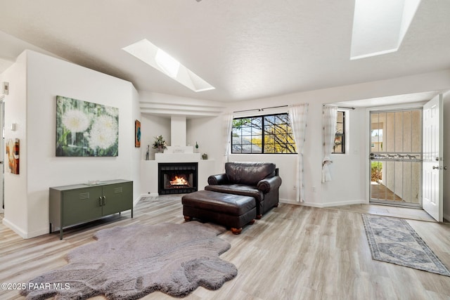 living room featuring wood finished floors, a warm lit fireplace, and a skylight