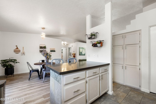 kitchen featuring light wood-style floors, dark countertops, baseboards, and vaulted ceiling
