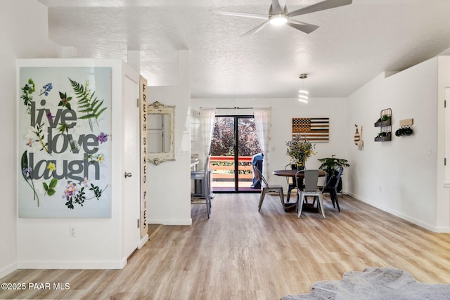 dining room featuring a textured ceiling, ceiling fan, baseboards, and light wood-type flooring