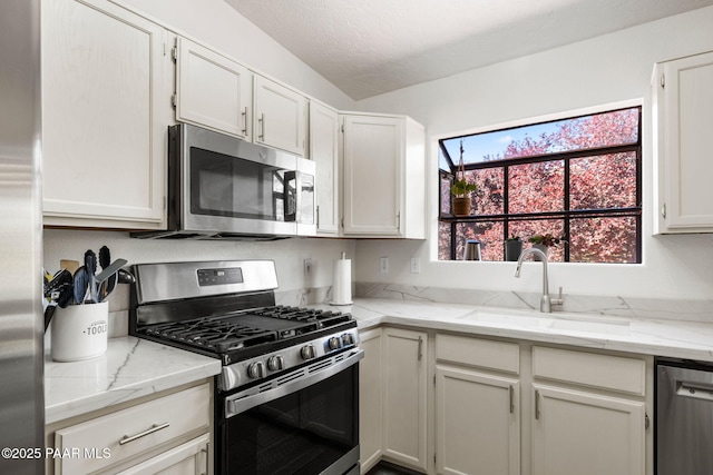 kitchen with light stone countertops, a textured ceiling, white cabinets, a sink, and stainless steel appliances