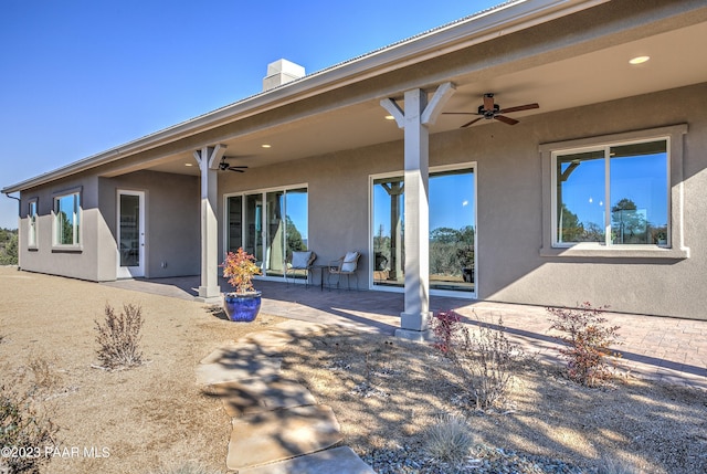 rear view of house featuring a ceiling fan, a chimney, stucco siding, and a patio