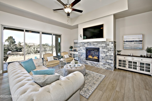 living room featuring wood finished floors, a glass covered fireplace, and a ceiling fan