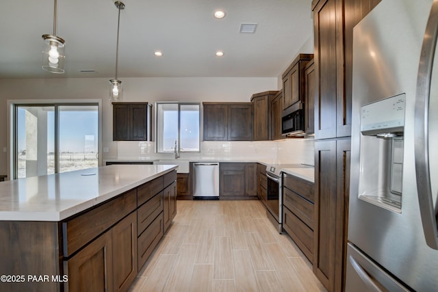 kitchen with appliances with stainless steel finishes, hanging light fixtures, backsplash, a center island, and dark brown cabinetry