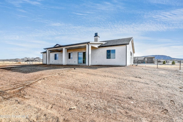 rear view of property with stucco siding, a mountain view, a chimney, and fence