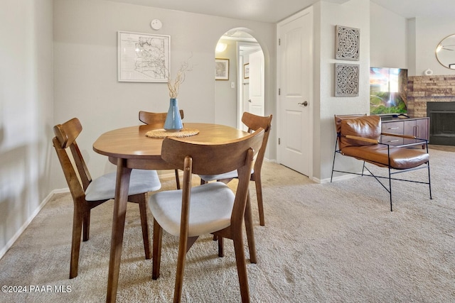 dining room featuring light carpet, a brick fireplace, baseboards, and arched walkways