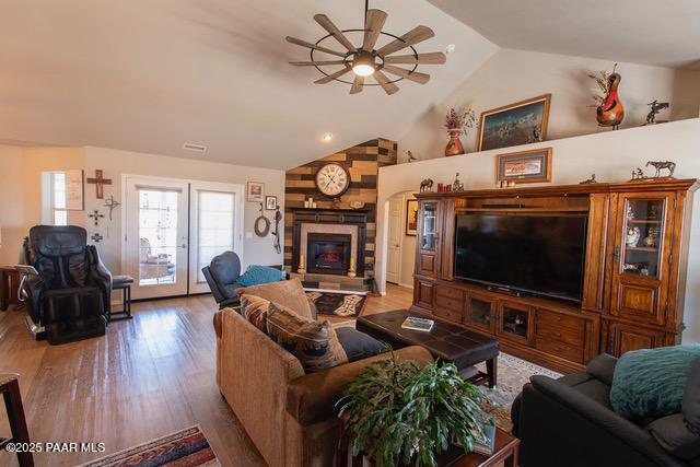 living area with a large fireplace, lofted ceiling, french doors, wood finished floors, and a ceiling fan