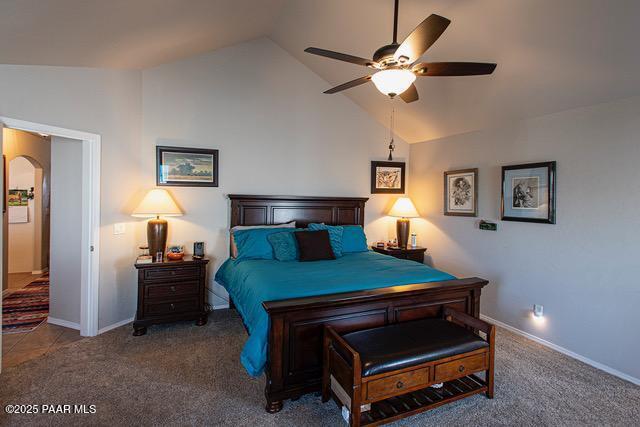 carpeted bedroom featuring vaulted ceiling, baseboards, arched walkways, and ceiling fan