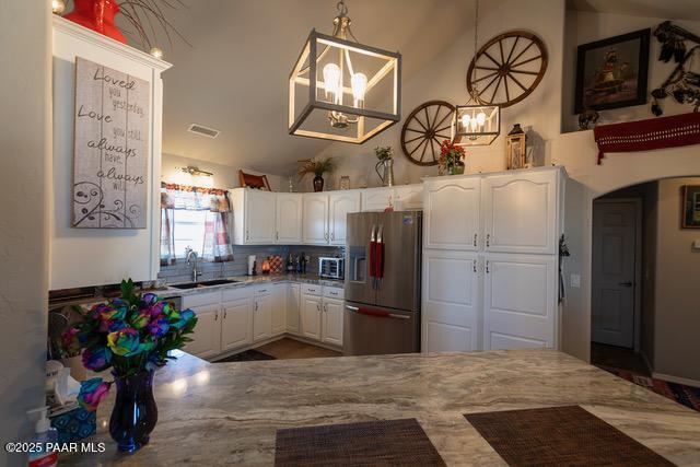 kitchen featuring visible vents, a sink, white cabinetry, stainless steel appliances, and vaulted ceiling