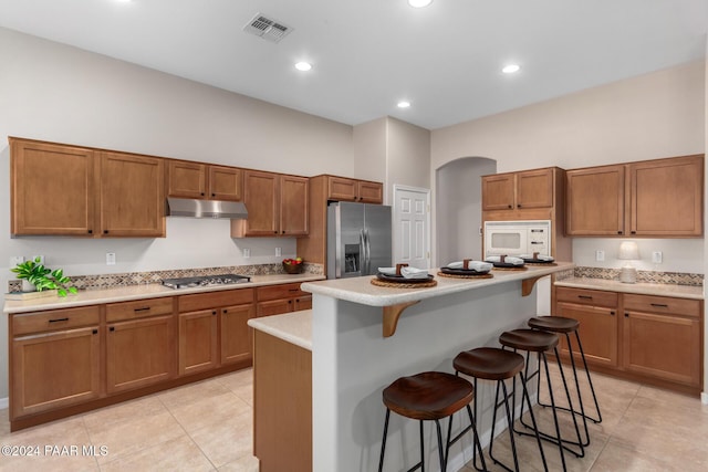 kitchen with a breakfast bar area, a kitchen island, stainless steel appliances, and light tile patterned floors