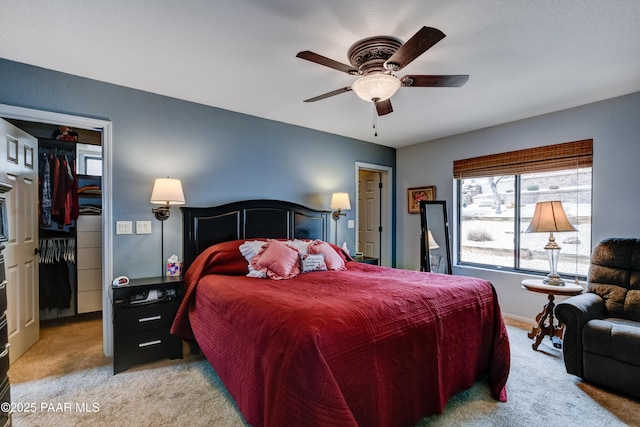 carpeted bedroom with a closet, baseboards, a walk in closet, and a ceiling fan